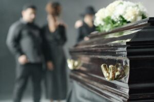 a coffin with a bouquet of white flowers with loved ones standing in the back.